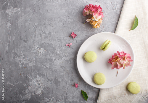Green macarons or macaroons cakes on white ceramic plate on a gray concrete background top view.