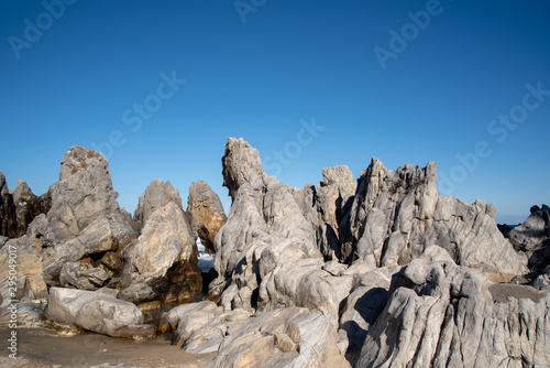 A cloudless blue sky and sea rocks of various shapes.