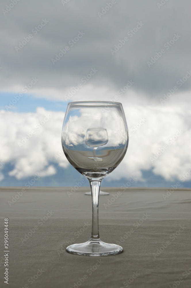 Empty transparent glass on beige table, in which reflected white clouds