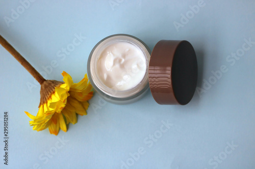 Bottle moisturizer for the face next to a yellow flower on a light blue background.