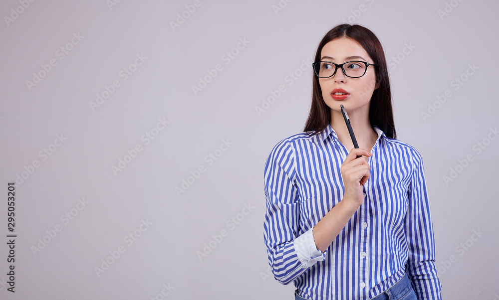 In the background is a pleasant young business woman with dark hair and computer glasses. girl holds a black pen in her hand. looking thoughtfully to the side In the background is a pleasant young business woman with dark hair and computer glasses. girl holds a black pen in her hand. looking thoughtfully to the side