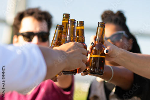 Diverse team of friends drinking beer outdoors. Hands of young men and women holding bottles and toasting. Celebration concept