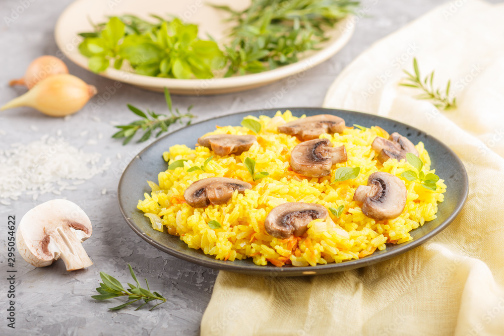 Yellow fried rice with champignons mushrooms, turmeric and oregano on blue ceramic plate on a gray concrete background. side view, selective focus.