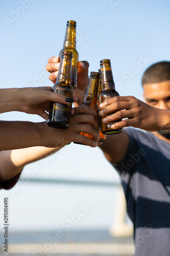 Group of people clinking bottled beer outdoors. Hands of young men and women holding bottles and toasting. Cheers concept