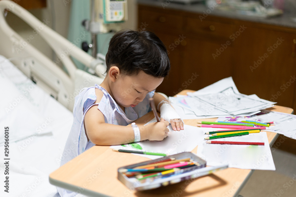The patient boy is painting the paper with a color pencil in the hospital. The patient boy is painting the paper with a color pencil in the hospital.