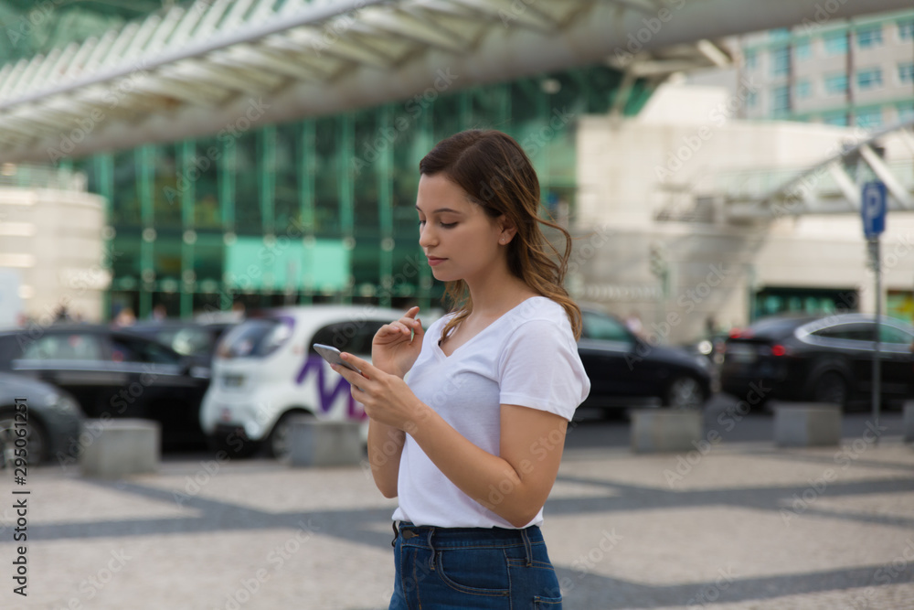 Attractive young lady using phone. Beautiful relaxed woman standing on city street with smartphone. Technology concept