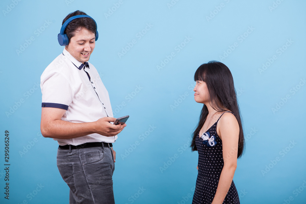 Smiling caucasian boyfriend with headphones ignoring his asian girlfriend Smiling caucasian boyfriend with headphones ignoring his asian girlfriend
