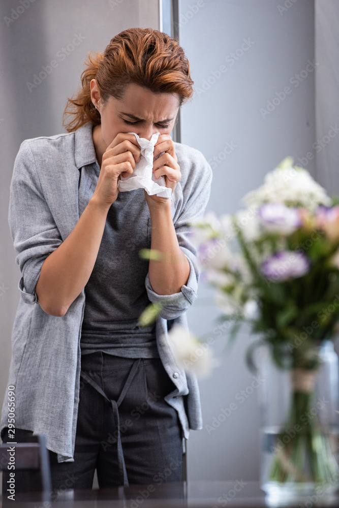 selective focus of woman sneezing in tissue near flowers in vase selective focus of woman sneezing in tissue near flowers in vase