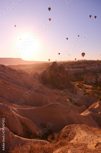 sunrise photo in Cappadocia with air balloons in the sky over sandy hills and a girl standing on the ground