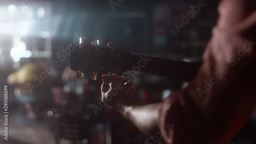 Close-up of a man tuning his acoustic guitar and starts to play in a dimly lit bar with a lens flare