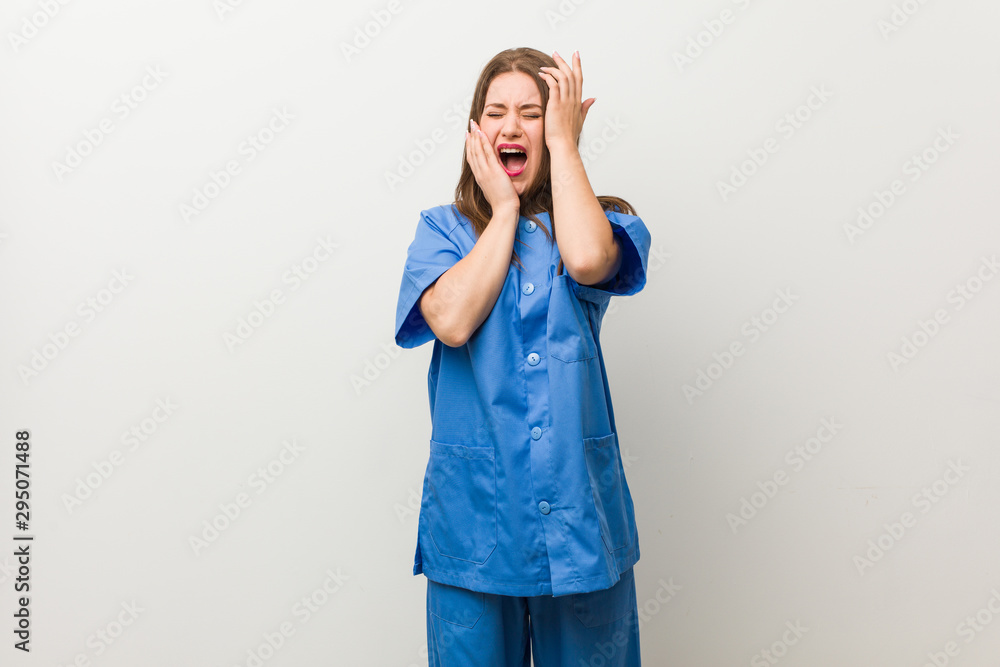 Young nurse woman against a white wall whining and crying disconsolately. Young nurse woman against a white wall whining and crying disconsolately.