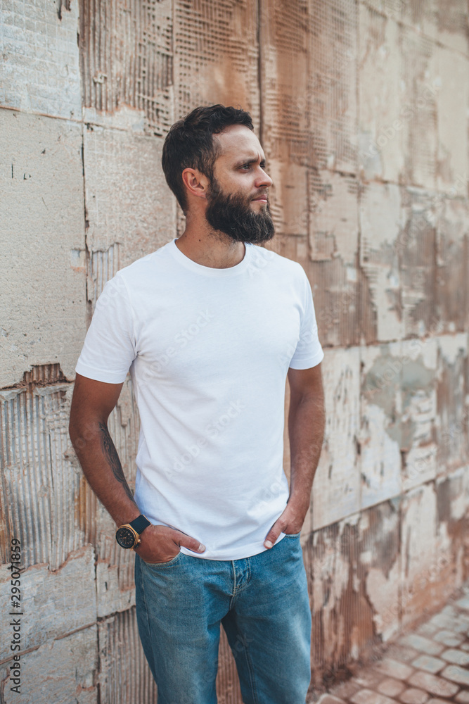Young hipster man with beard wearing white blank t-shirt and blue jeans outdoor. Young hipster man with beard wearing white blank t-shirt and blue jeans outdoor.