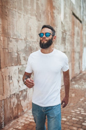 Young hipster man with beard wearing white blank t-shirt and blue jeans outdoor.