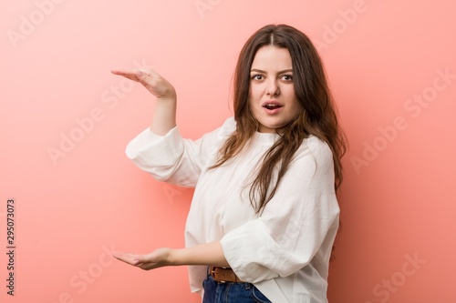Young caucasian curvy woman standing against pink background