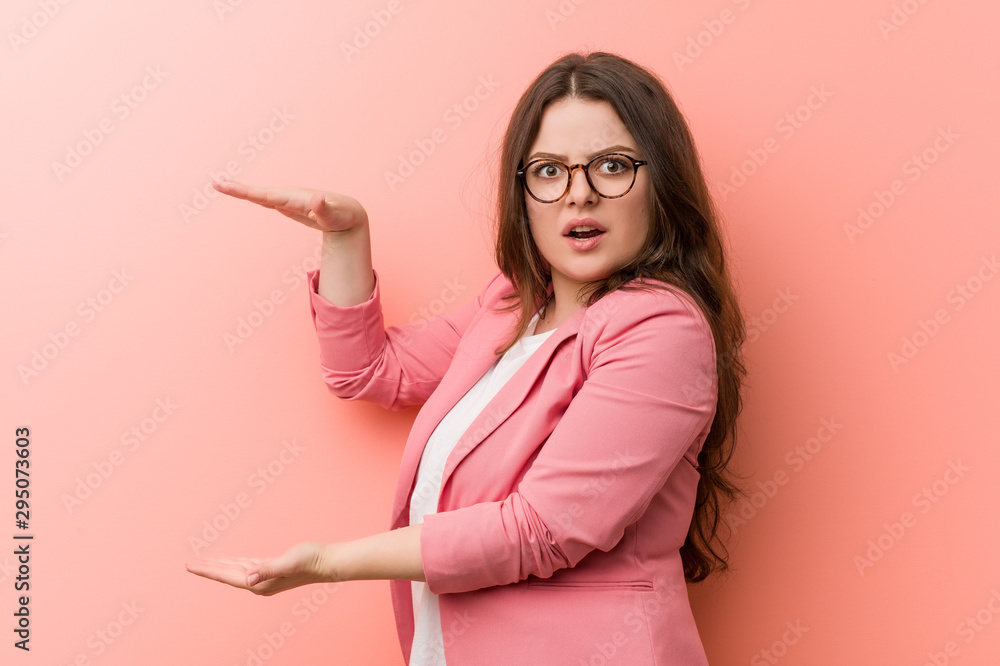 Young plus size business caucasian woman shocked and amazed holding a copy space between hands. Young plus size business caucasian woman shocked and amazed holding a copy space between hands.