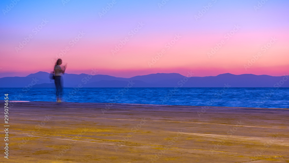 Sunset over Aegean Sea in Aegina Island and a girl on the wharf, Greece, Long exposition, motion blur