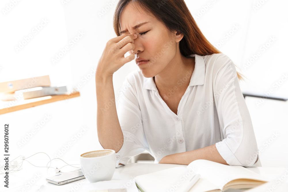 Image of exhausted asian businesswoman rubbing her nose in office Image of exhausted asian businesswoman rubbing her nose in office
