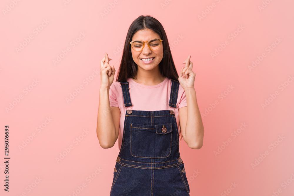 Young pretty arab woman wearing a jeans dungaree crossing fingers for having luck Young pretty arab woman wearing a jeans dungaree crossing fingers for having luck