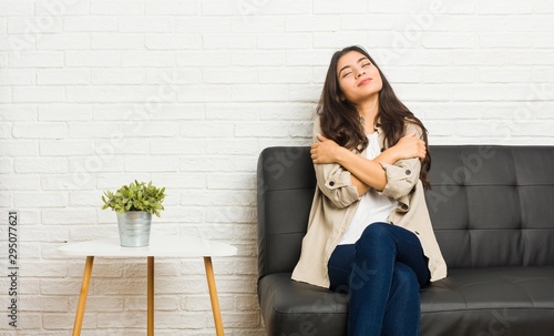 Young arab woman sitting on the sofa hugs, smiling carefree and happy. photo