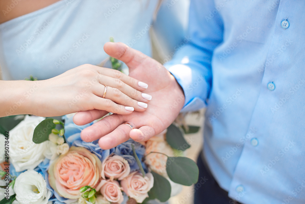Fototapeta premium Groom wears bride a wedding ring Bride hand holds a beautiful wedding bouquet