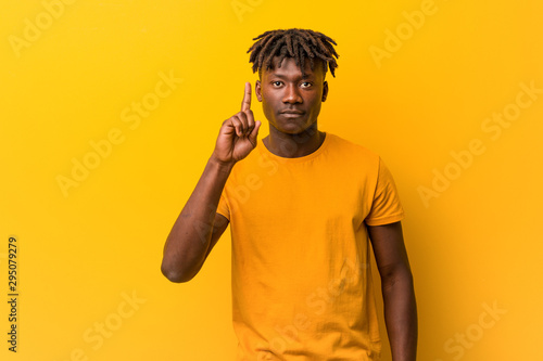 Young black man wearing rastas over yellow background showing number one with finger.