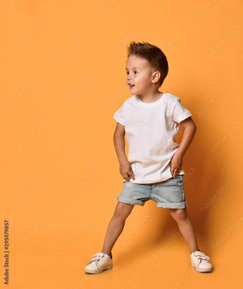 Excited kid boy in white t-shirt and blue shorts is looking at something on free copy space on yellow is ready to run Excited kid boy in white t-shirt and blue shorts is looking at something on free copy space on yellow is ready to run