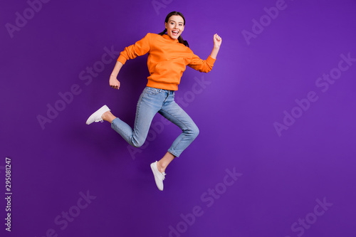Full body photo of positive cheerful youth girl jump run after discounts feel content wear sportswear denim jeans white sneakers isolated over violet purple color background