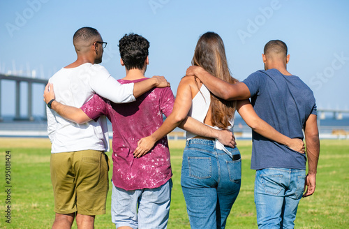 Team of friends embracing outside. Backs of young men and woman standing in line on grass, hugging each other. Friendship or unity concept