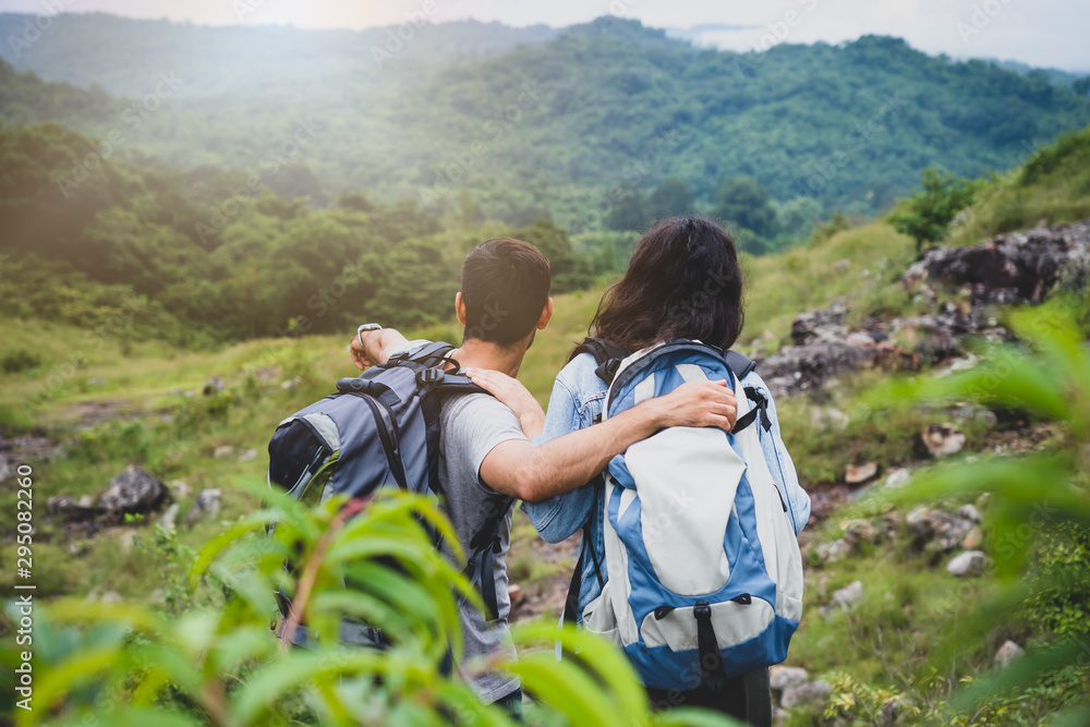 Two travelers with backpacks hugging each other and enjoying the view of the valley and friendship.