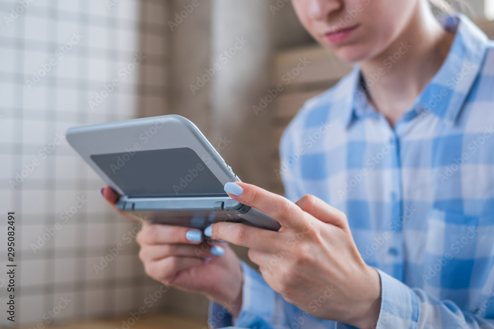 Close up view of woman hand using grey handheld game console at bright living room. Gaming, hobby, technology, entertainment, portable, video game and leisure time concept Close up view of woman hand using grey handheld game console at bright living room. Gaming, hobby, technology, entertainment, portable, video game and leisure time concept