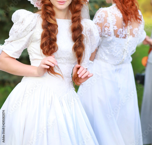 beautiful girsl in a white dress with red braids on nature in the company of girlfriends photo