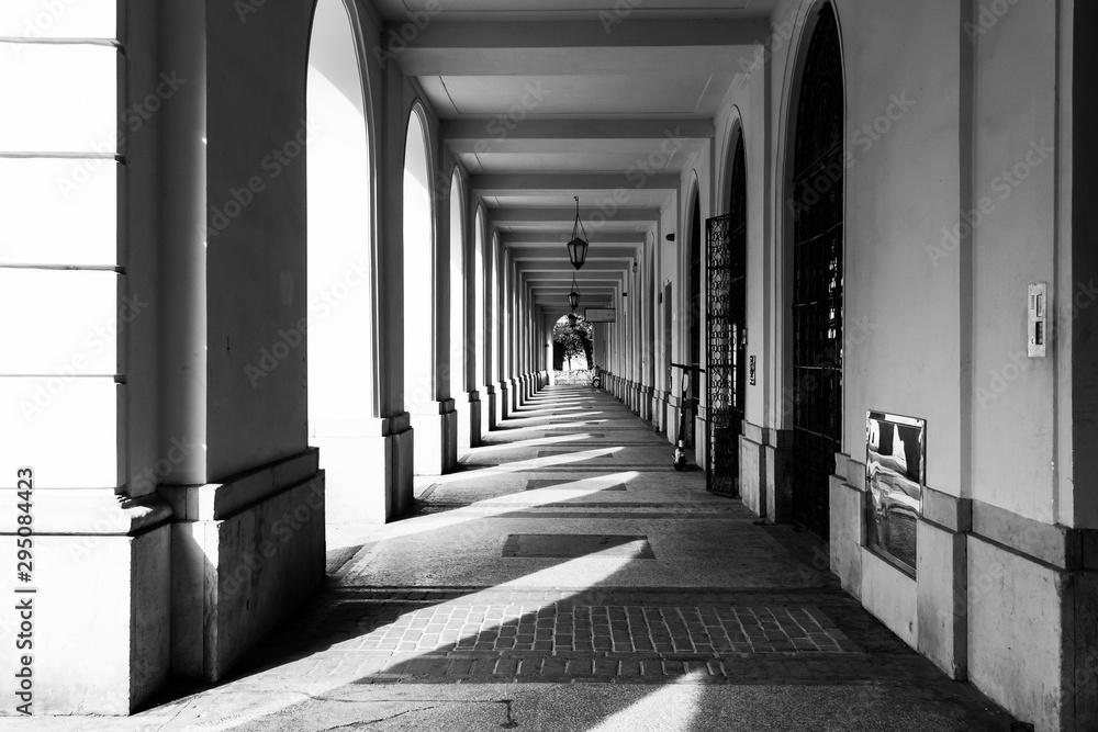 Arcades with shadows of columns on the pavement - covered walkway enclosed by a line of arches outside the building on a sunny day. 