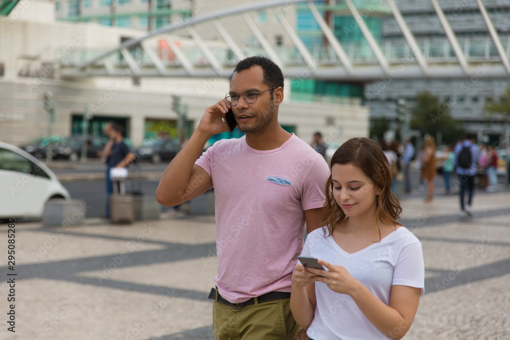 Front view of two people walking on street with smartphones. Handsome African American man talking on phone while walking on street with friend. Communication and technology concept