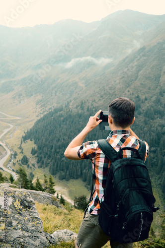 young man takes pictures on a cell phone and enjoying mountain landscape, the concept of hiking with lightweight modern gadgets for photographing travel and lifestyle, outdoor adventure