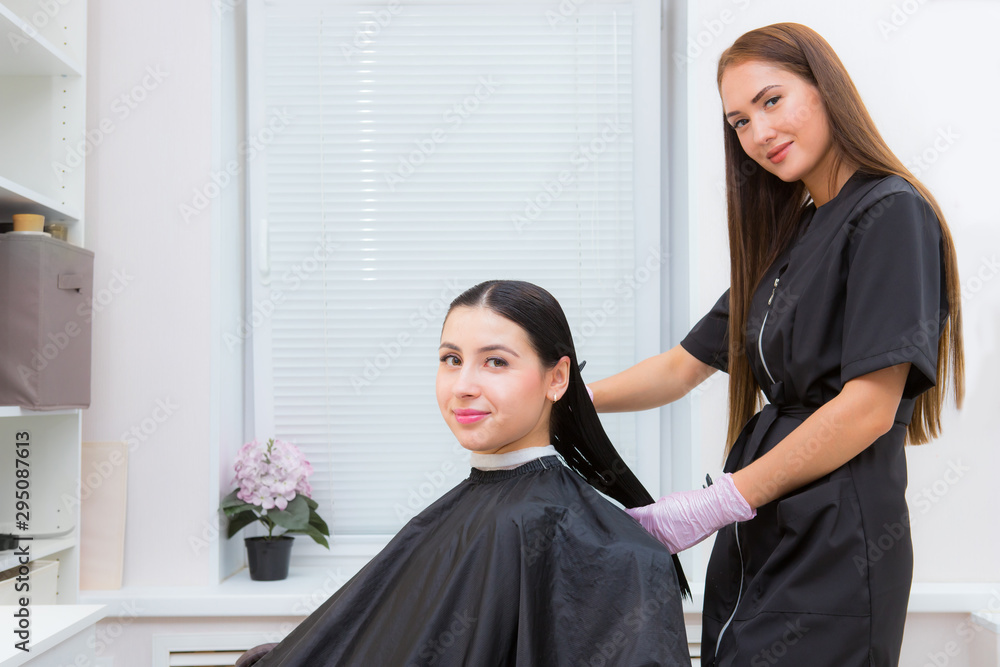 Happy young woman and hairdresser. The hairdresser applies the product on the client's long hair Happy young woman and hairdresser. The hairdresser applies the product on the client's long hair