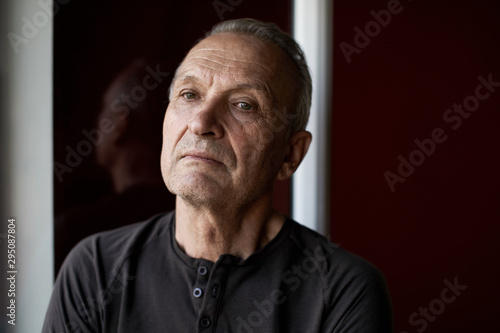 Portrait of serious handsome elderly man with gray hair, stylishly dressed , looking at camera against the background of window