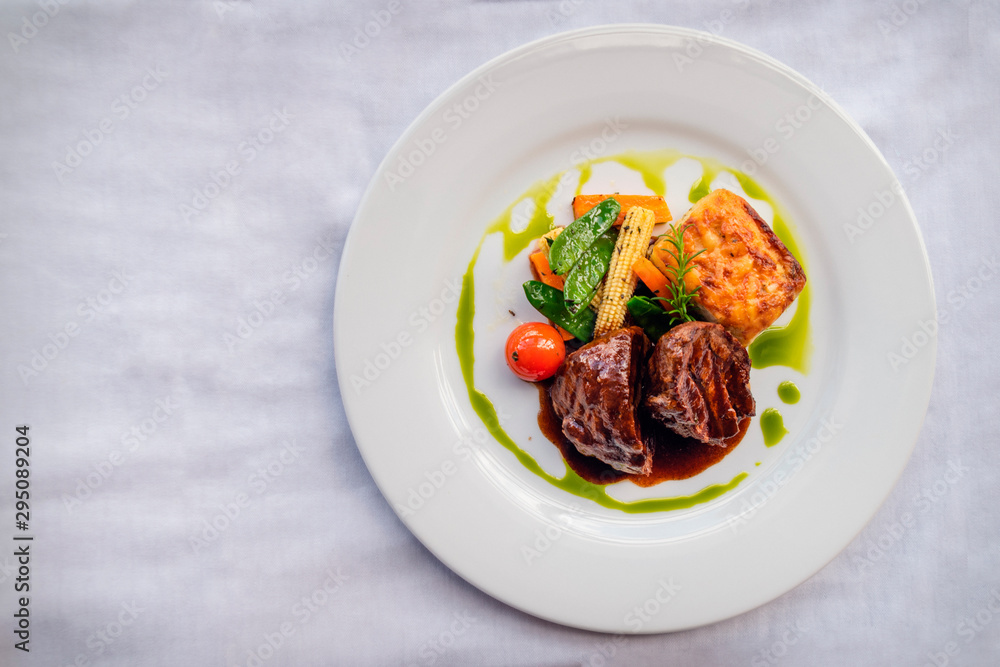 Grilled beef tenderloin medallions, served with potatoes and baby vegetables, and bathed in a braised pepper sauce. White background. Top view Grilled beef tenderloin medallions, served with potatoes and baby vegetables, and bathed in a braised pepper sauce. White background. Top view