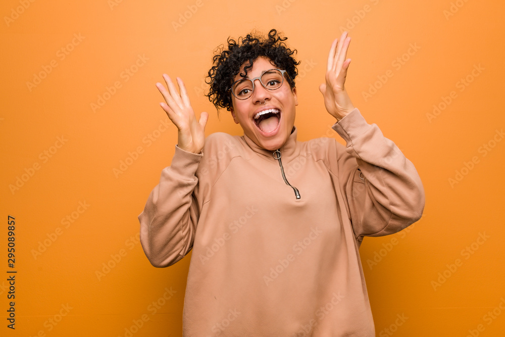 Young mixed african american woman against a brown background celebrating a victory or success, he is surprised and shocked. Young mixed african american woman against a brown background celebrating a victory or success, he is surprised and shocked.