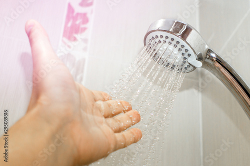 male hand under the stream of water from the shower head, fixed in the holder, checks the water temperature in the bathroom