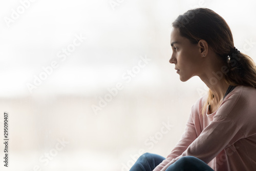 Thoughtful pensive girl sitting alone looking through window photo