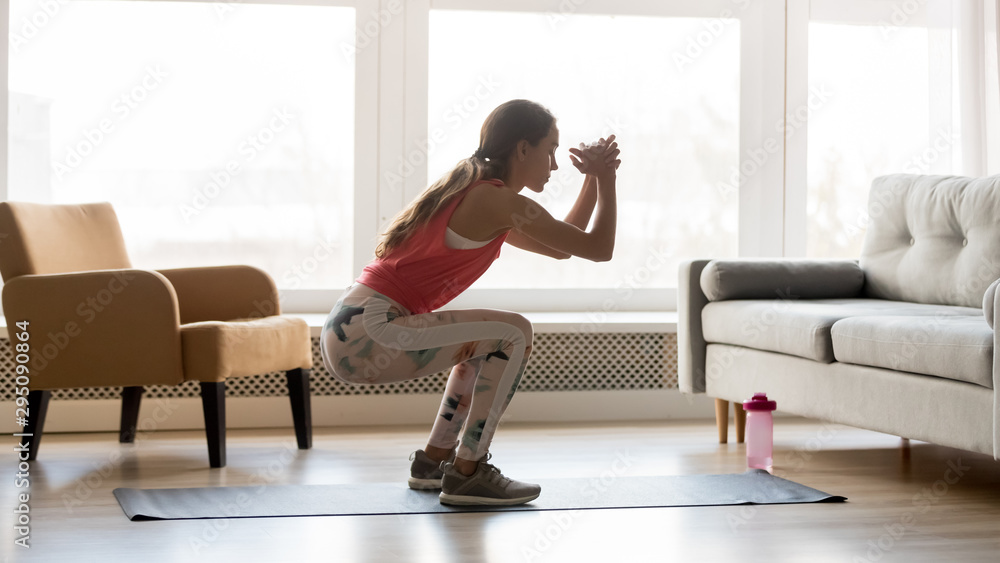 Sporty young woman doing squat morning exercise in living room