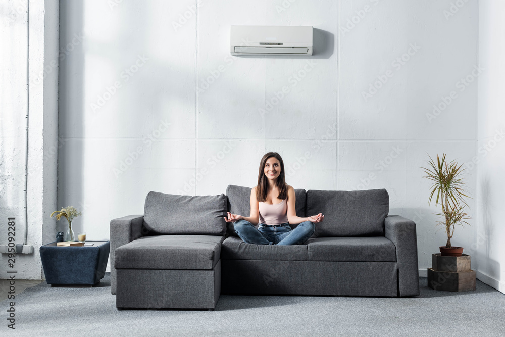 attractive and smiling woman in lotus pose sitting on sofa attractive and smiling woman in lotus pose sitting on sofa