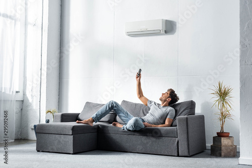 handsome man lying on sofa and switching on air conditioner photo