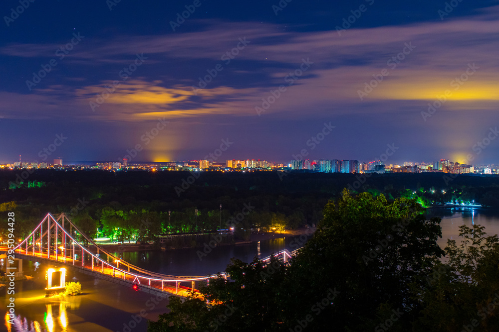 Fototapeta premium Night city landscape. A bridge across the river with bright colored lights. Landscape of the city in the night