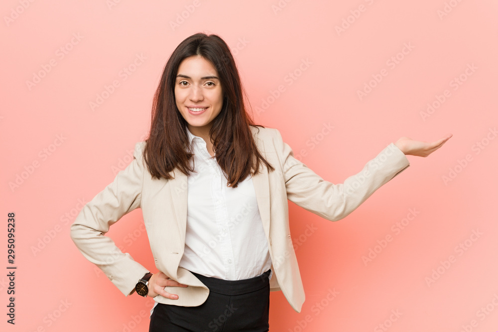 Young brunette business woman against a pink background showing a copy space on a palm and holding another hand on waist. Young brunette business woman against a pink background showing a copy space on a palm and holding another hand on waist.