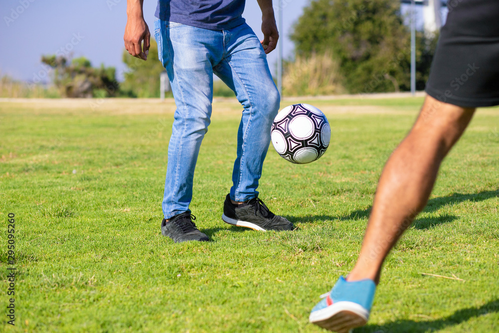 People playing soccer in park. Legs of man in casual jeans kicking football ball on grass. Outdoor activity concept People playing soccer in park. Legs of man in casual jeans kicking football ball on grass. Outdoor activity concept