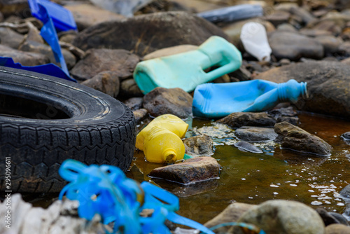Earth plastics pollution global enviroment emergency. Old car tire in dirty water stream with plastic bottles and trash.