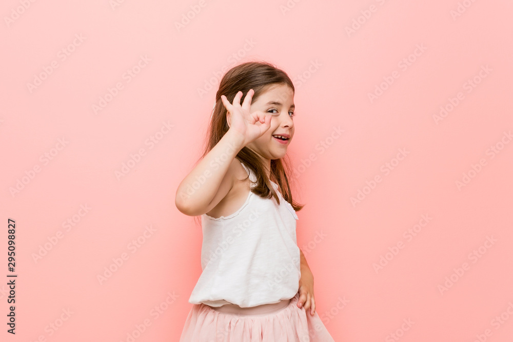 Little girl wearing a princess look winks an eye and holds an okay gesture with hand. Little girl wearing a princess look winks an eye and holds an okay gesture with hand.