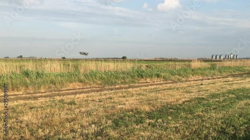 An agricultural airplane crop duster, flies low above the ground and sprays chemicals, then crosses the highway and flies off the frame.