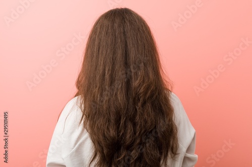 Young caucasian curvy woman standing in a backward position against pink background